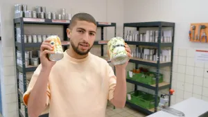 Een foto van de presentator die twe eblikjes met groente in zijn handen omhoog houdt.