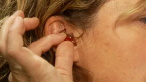 Foto van oor waar een hand een gekleurd oordopje in doet ter bescherming van het oor.