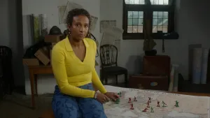 Een still van de presentator die op een oude zolder staat. Er liggen in de achtergrond allemaal props uit de Eerste Wereldoorlog en er is een kaart van Europa te zien, waar groene en rode soldaatjes op staan.