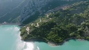 Foto van kustlijn in Albanie, heuvel met slingerende weg tussen bomen aan een azuurblauwe zee.