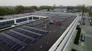Een foto in vogelperspecitief van een groot pand met plat dak dat vol ligt met zonnepanelen.