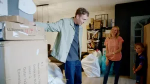 Een man staat met een hand op een doos in de woonkamer van een vrouw.