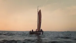 Een foto van een vissersboot op zee met op de achtergrond windmolens.