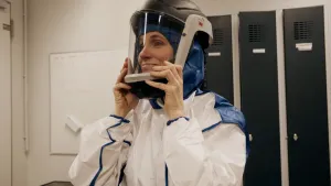 Foto van presentatrice Petra Grijzen die in een wit pak en helm met kijkvenster bij zichzelf opzet, in voorbereiding op een maanwandeling op aarde.