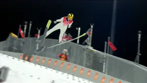 Foto van een skispringer op de Olympische Spelen in de lucht met de ski's in V-vorm voor zich.