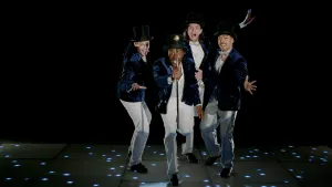 Foto van vier jongens in showpak op een podium met microfoon.