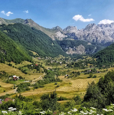 Foto van bergachtig landschap in ALbanie, begroeid met bomen en blauwe lucht erboven.