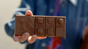 Foto van hand die een chocoladereep laat zien waarop verschillende vormpjes zijn gedrukt, zoals een strik.