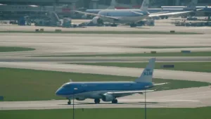Een foto van een vliegtuig op een startbaan op Schiphol, op de achtergrond staan andere vliegtuigen.