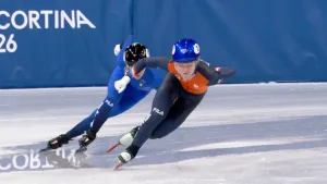 Foto van twee shorttrackers die net uit de bocht komen, met een hand op hun rug en de andere in de lucht.