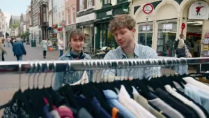Een foto van twee mensen op straat die naar een kledingrek kijken.