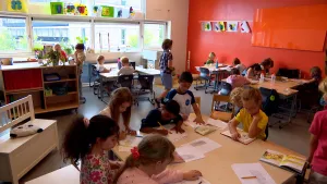 Foto van basisschoolklas waarin kinderen in groepjes zitten en tekeningen aan een rode muur hangen.