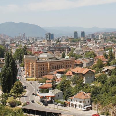 Panoramafoto van de stad Sarajevo met veel groen en een rivier.
