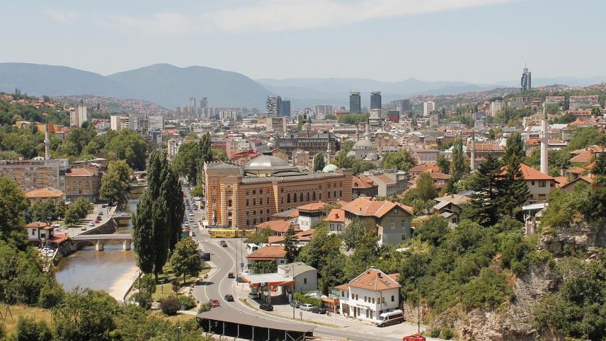 Panoramafoto van de stad Sarajevo met veel groen en een rivier.