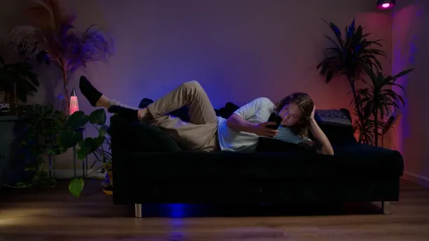 Foto van Klokhuispresentator Pascal die op de bank naar zijn smartphone kijkt.