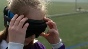 Foto van meisje dat grote zwarte bril op haar gezicht doet, ze staat op een voetbalveld want ze doet mee aan blindenvoetbal.
