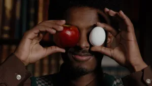 Foto van presentator Anas met voor zijn ogen een rode appel en een wit ei.