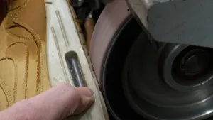 Closeupfoto van gele sneaker waarvan de zool door een schoenmaker geschuurd wordt met een bandschuurapparaat.