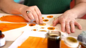 Foto van de handen van illustrator Djenne Fila die bezig is met de losse onderdelen van een oranje vlinder.