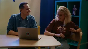 Foto van presentatrice Janouk aan een bureau met Joris van Pointer, ze bekijken nepnieuwsfilmpjes op een laptop.