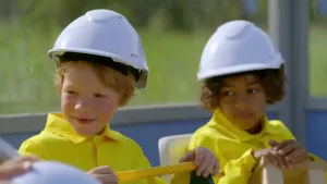 Foto van twee jongetjes met bouwhelmen op en gele overalls aan