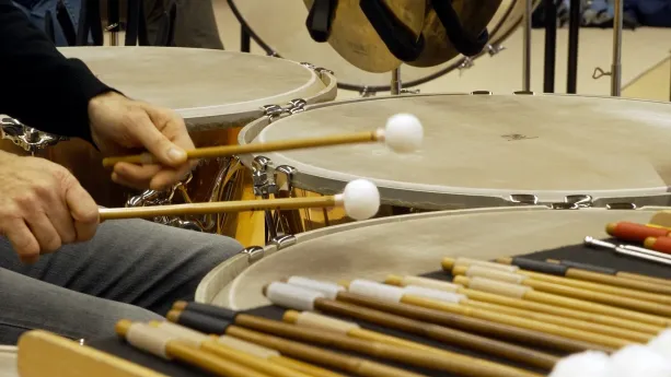 Foto van handen van paukenist die met stokken op grote ronde trommels slaat.