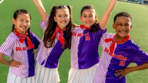 Foto van vier kinderen in sportkleding op een groen sportveld, ze kijken blij.