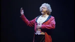 Foto van een meneer die fluitend in een kostuum op een podium staat