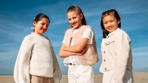 Foto van drie meisjes in witgetinte kleren op het strand voor blauwe lucht.