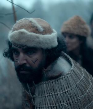 Foto van jagers uit de prehistorie die gespannen kijken naar een prooi. Man met donker haar, baard, bruine muts en tekening op het gezicht loopt voorop.