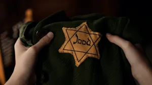 Foto van twee handen die een groene jas vasthouden waarop een gele jodenster is genaaid.