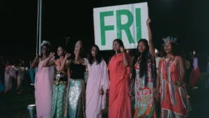 Foto van Surinaamse vrouwen in feestelijke gewaden die een bord met daarop het woord 'fri' omhoog houden, tijdens de onafhankelijkheid van Suriname in 1975.