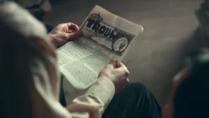 Foto van handen die verzetskrant Trouw vasthouden, een gelig blaadje met kleine lettertjes en bovenaan een grote header met in hoofdletters TROUW.