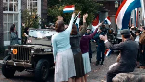 Foto van mensen die met Nederlandse vlaggen de geallieerden toejuichen die in jeeps door de straten rijden, anno 1945.
