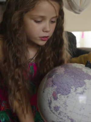 Meisje in een jurkje zit op een bank en kijkt naar een wereldbol.