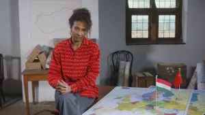 Presentatrice Astrid zit op een tafel. Naast haar ligt een kaart van Europa met daarop vlaggetjes.