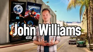 Foto van presentator Sander Zwiep voor een Amerikaanse filmstudio met filmposters van ET, Superman, Harry Potter en Star Wars en de naam John Williams in beeld.