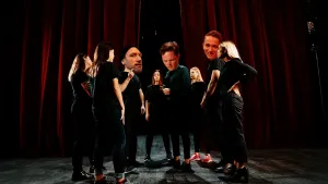 Foto van toneel met rode gordijen waarop mensen staan te zingen als koor.