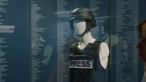 Een pop in een vitrine draagt een kogelvrij vest met daarop het woord 'press'
