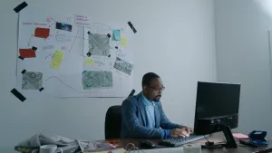 Een onderzoeksjournalist zit achter een computer. Achter hem hangen aanwijzingen.