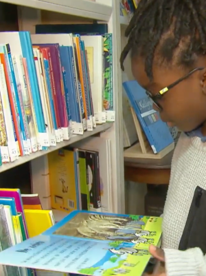 Een kind staat voor een boekenkast in een kringloopwinkel en bladert door een boek met zebra's.