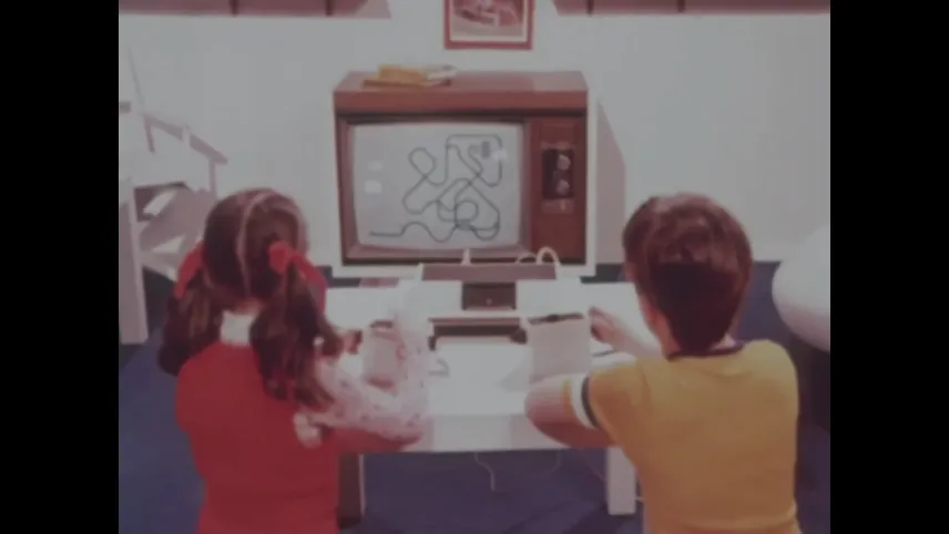 Foto van een jongen en een meisje achter de eerste spelcomputer, een ouderwetse bruine tv met een eenvoudig spelletje. Ze bedienen het spel met witte kastjes.