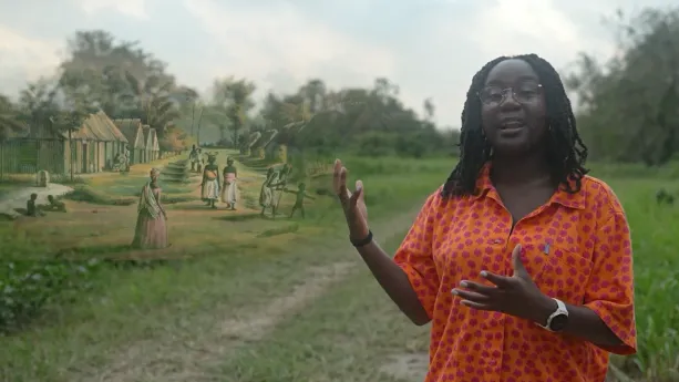 Presentator Tirsa staat in een groen veld. Links van haar is een plaatje te zien van huisjes op een plantage.