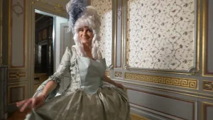 Presentatrice Janouk heeft een baljurk aan. Ze staat in een oude zaal met behang op de muren.