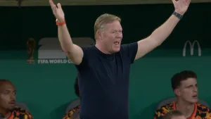 Foto van bondscoach Ronald Koeman die zijn armen in de lucht gooit tijdens een wedstrijd van het Nederlands elftal.