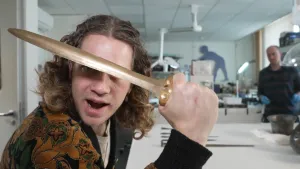 Een foto van presentator Pascal die een klein bronzen zwaard voor zijn gezicht houdt.