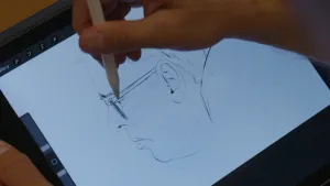 Een foto van een tekening van het gezicht van een man met bril van de zijkant gezien. De tekening wordt gemaakt op een tablet, een hand met een tekenpen zweeft boven de tablet.