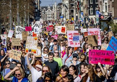 Foto van protestmars voor vrouwenrechten, mensen houden borden vast met feministische leuzen.