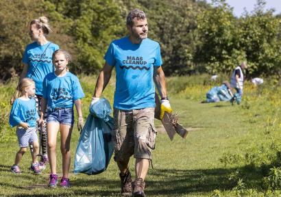 Foto van mensen in blauwe shirts die met volle vuilniszakken door natuurgebied lopen om zwerfvuil op te ruimen.