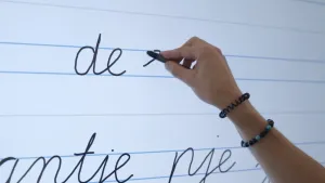 Een foto van een hand die letters op een digibord schrijft. Er staat al 'de', het volgende woord dat wordt geschreven begint met een 'e'. Er wordt netjes tussen de lijntjes geschreven.